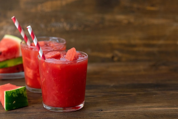 Verre de smoothie pastèque avec des tranches de pastèque fraîches sur fond de bois foncé