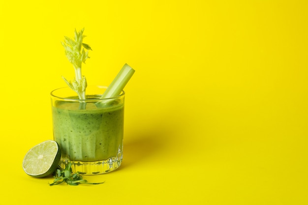 Verre de smoothie vert et ingrédients sur table jaune