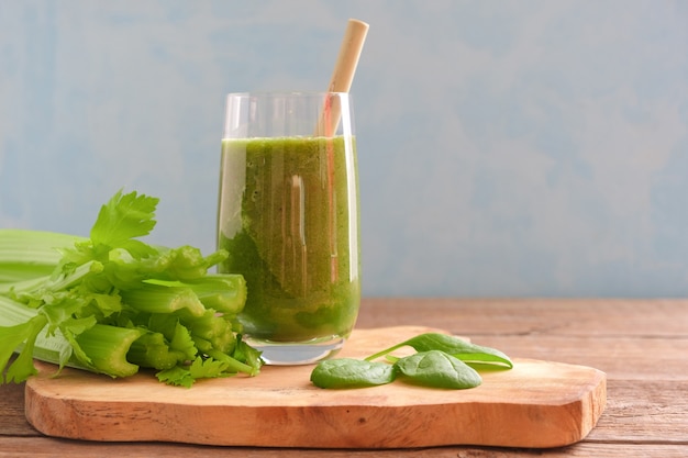 Un verre avec un smoothie vert et une paille à cocktail en bambou est posé sur une planche de bois.