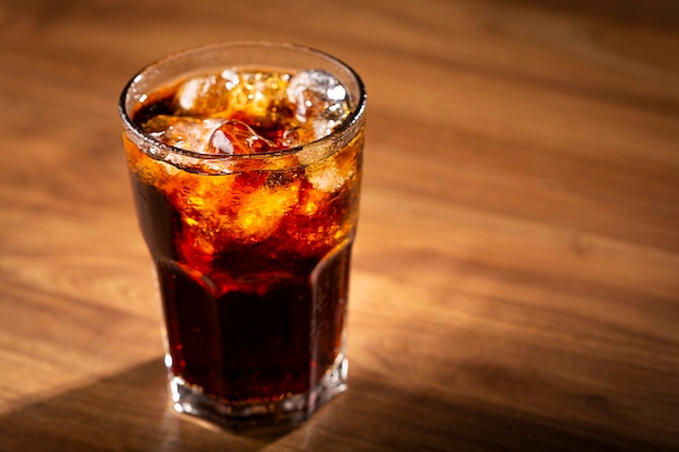 Verre de soda au cola avec des glaçons sur une table en bois