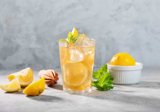 Verre de thé glacé au citron sur fond gris béton avec menthe et glace