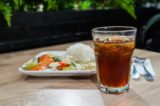 Un verre de thé glacé est posé sur une table à côté d'une assiette de nourriture.