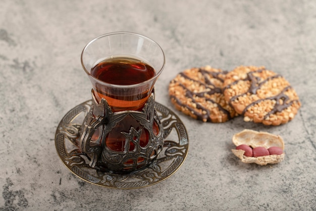 Verre de thé noir, cacahuètes et biscuits sucrés sur pierre.