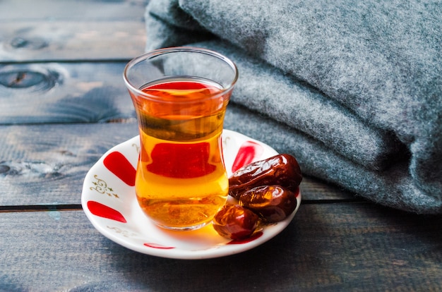 Un verre de thé noir et des dates sur une soucoupe