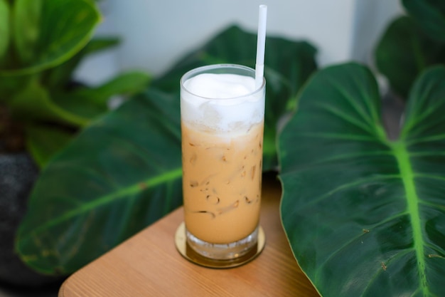 Verre de thé thaïlandais glacé sur table en bois avec fond de feuilles vertes.