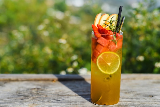 Verre de thé tropical vert avec citron vert, orange, pastèque et pomme sur fond vert d'été