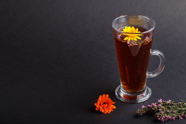 Verre de tisane avec calendula et hysope sur fond noir. Vue latérale, espace copie.