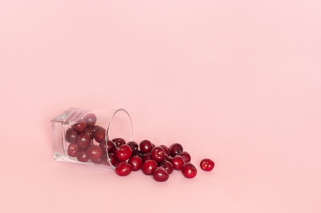 Verre tombé avec des cerises dispersées sur fond rose.