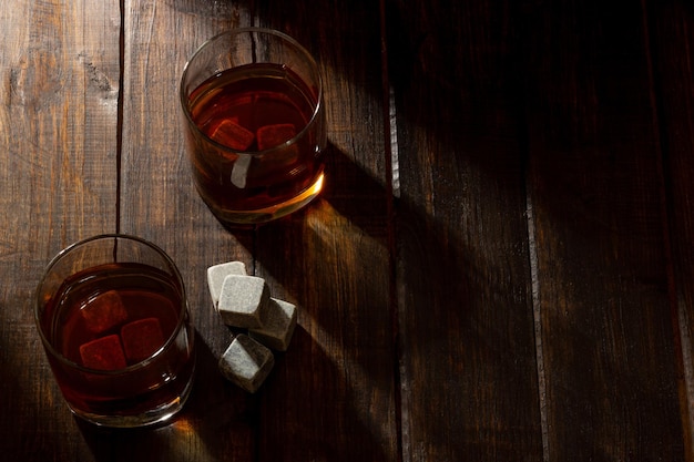 Verre transparent avec du whisky sur un fond en bois foncé avec des rayons lumineux de lumière Pierres de whisky dans l'épicerie