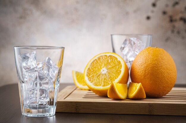 Verre transparent vide avec des glaçons. Sur un mur en bois avec des fruits orange