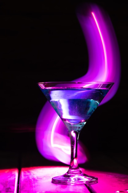 Verre triangulaire avec un cocktail bleu sur fond sombre et éclairage au néon.