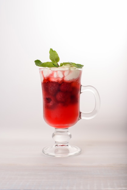 Un verre en verre avec une boisson framboise froide avec de la crème fouettée et de la menthe sur le dessus.