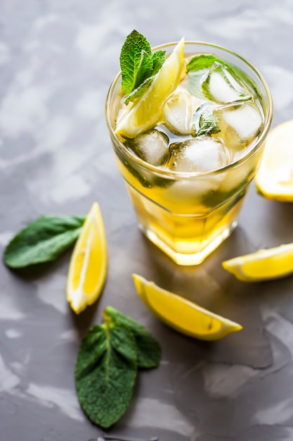 Un verre de verre avec un thé froid avec glace, menthe et citron sur un fond de béton gris.