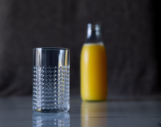 Verre vide sur la table. En arrière-plan, une bouteille pleine de jus est floue.