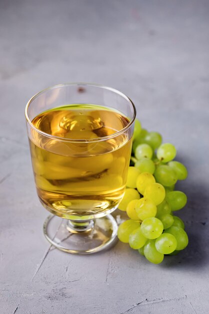 Verre de vin blanc et branche de raisins verts sur fond gris vertical