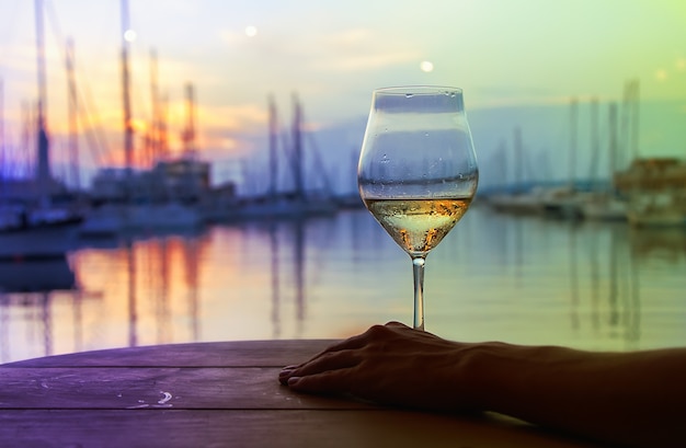 le verre de vin blanc sur fond de déclin du soleil dans le port avec des yachts