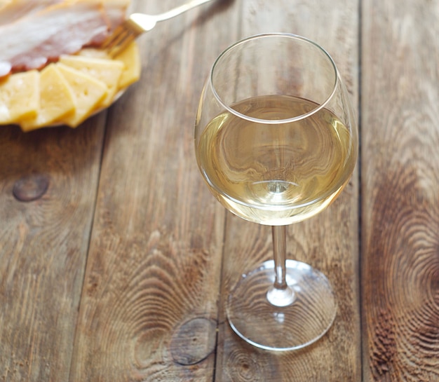 Photo un verre de vin blanc se dresse sur une table en bois, derrière une assiette de fromage et de bacon.