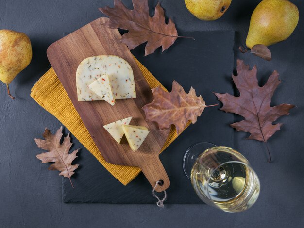 Photo un verre de vin blanc servi avec du fromage dans une planche à découper sur fond sombre