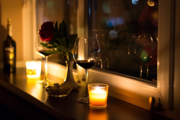 Un verre de vin, des bougies et une fleur près de la fenêtre. Soirée romantique à la maison