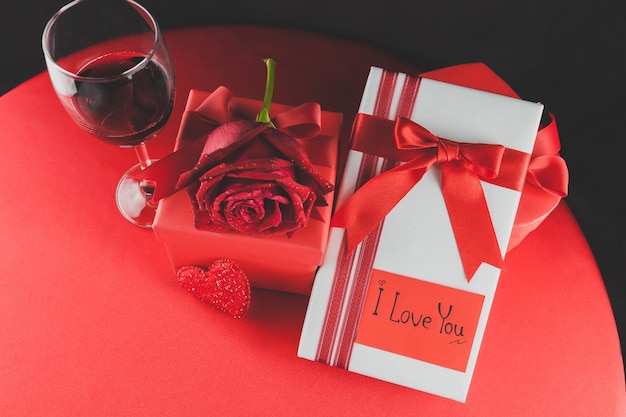 Un verre de vin avec des cadeaux et une rose sur une table rouge