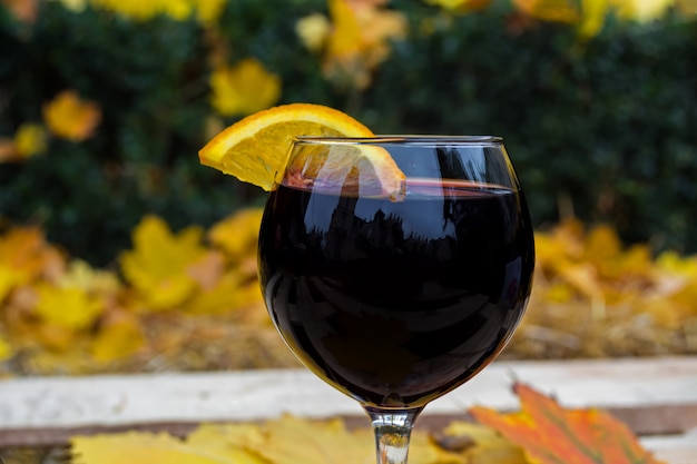 Un verre de vin chaud dans un automne froid, sur fond de feuilles jaunes et rouges