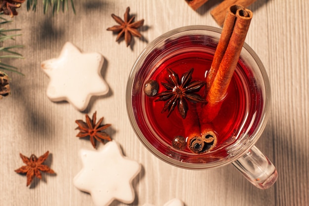 Verre de vin chaud de Noël à la cannelle, à l'anis étoilé et aux clous de girofle sur fond de bois avec des biscuits blancs, des branches de sapin naturel et des cônes. Vue de dessus. Effet tonifiant des couleurs.