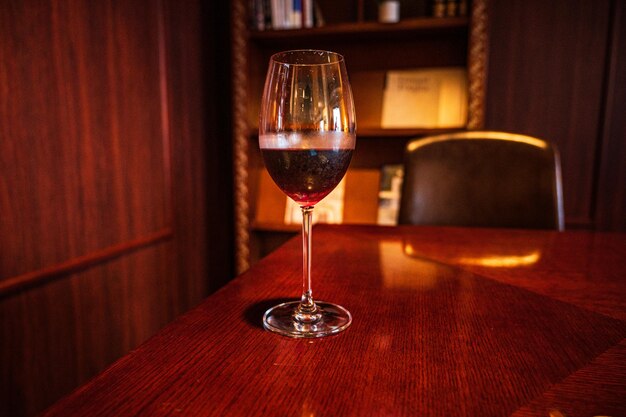 Un verre de vin est posé sur une table avec une bibliothèque derrière.