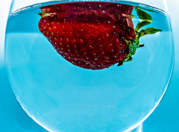 Verre de vin à la fraise flottant sur fond bleu.