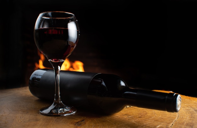 Verre à vin plein et bouteille de vin allongé sur une surface en bois rustique avec feu derrière