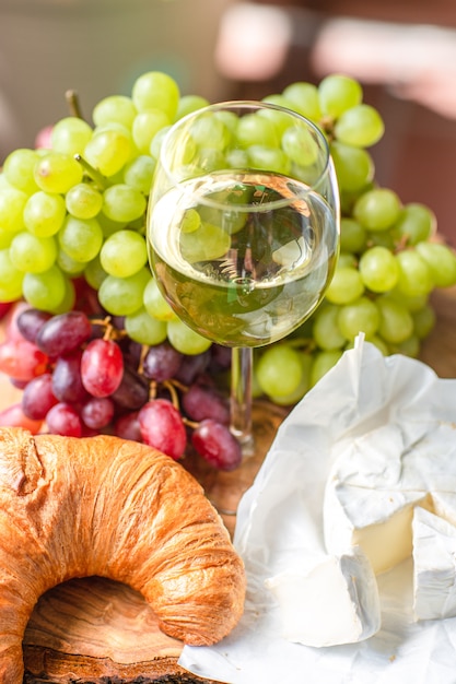 Photo un verre de vin avec des raisins rouges et verts, du fromage et un croissant.