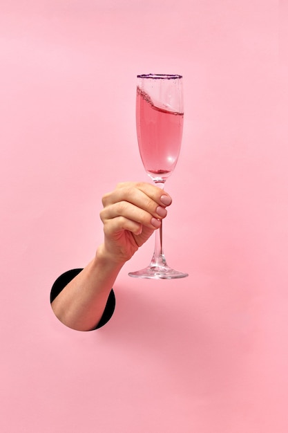 Verre à vin rose dans une main féminine du trou dans le mur