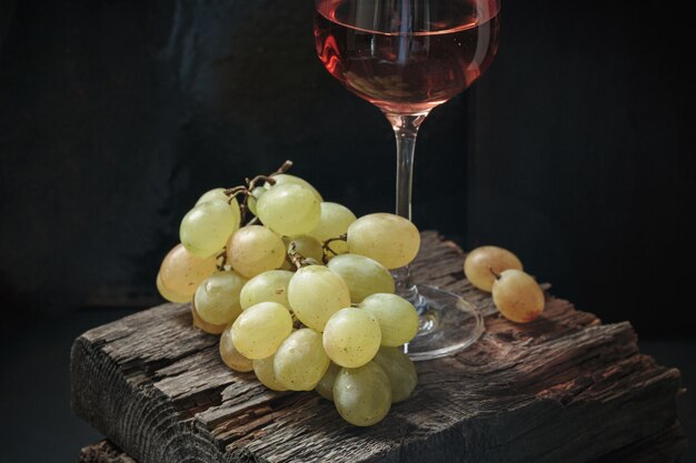 Un verre de vin de rose avec des raisins blancs mûrs sur un fond sombre
