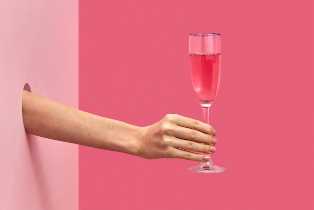 Verre de vin rose de vacances dans la main d'une femme à travers le trou dans le mur sur un fond rose bicolore avec des ombres douces, espace de copie. Notion de vacances.