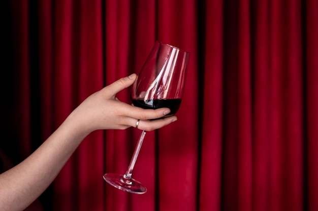 Un verre de vin rouge dans une main féminine sur un fond de texture rouge