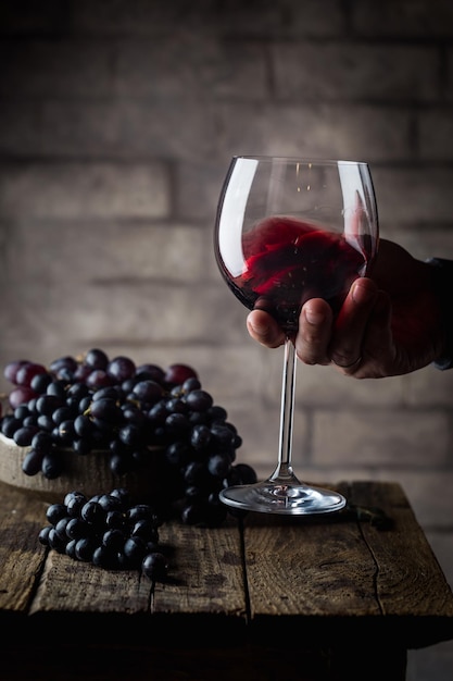 Verre à vin rouge dans une main d'hommes et raisins mûrs sur fond de bois