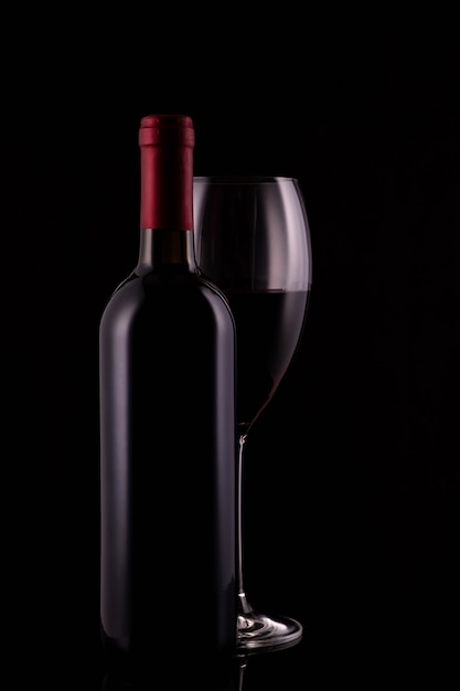 Verre à vin rouge élégant et bouteille de vin noir sur fond noir