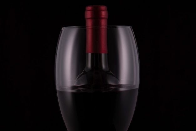 Verre à vin rouge élégant et bouteille de vin noir sur fond noir