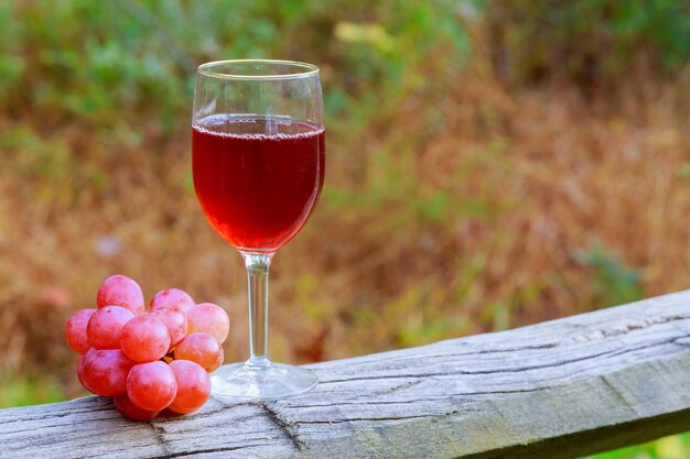 Verre à vin rouge et grappe de raisin sur table en bois contre vignoble en été