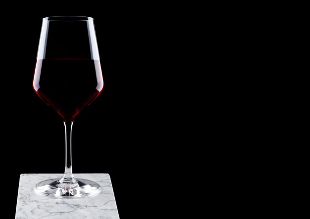 Verre de vin rouge sur planche de marbre blanc sur fond noir.