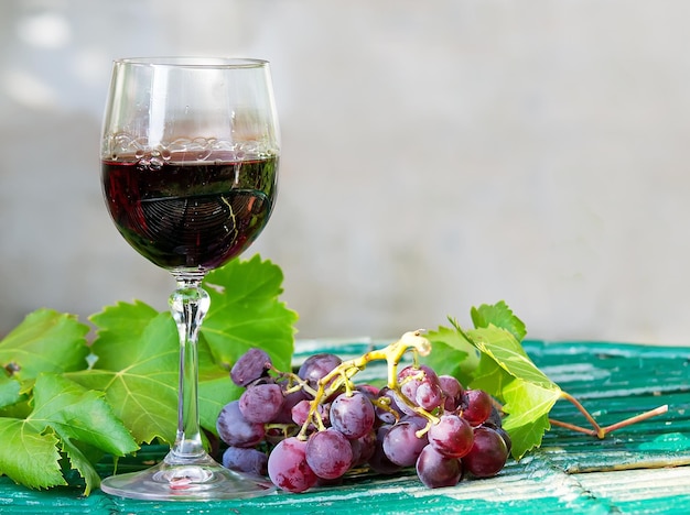 Verre de vin rouge avec des raisins et des feuilles sur une table en bois