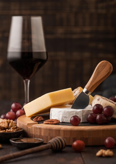 Verre de vin rouge avec sélection de divers fromages sur le plateau et raisins sur fond de table en bois Blue Stilton Red Leicester et Brie Fromage et couteau au miel