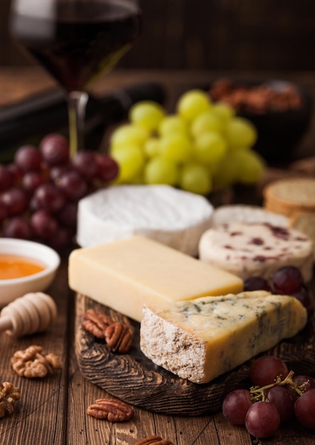 Verre de vin rouge avec sélection de divers fromages et raisins sur fond de table en bois Blue Stilton Red Leicester et Brie Fromage et couteau au miel