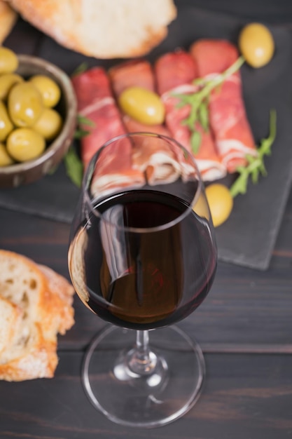 Verre de vin rouge avec des tranches de jambon cru ou espagnol jamon serrano ou italien prosciutto crudo pain olives vertes et roquette