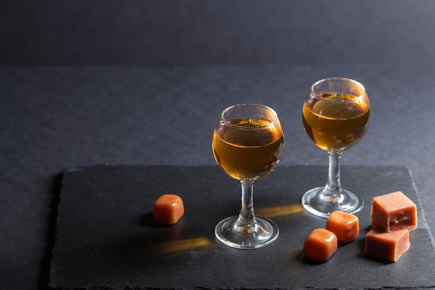 Verre de whisky avec des bonbons au caramel sur une ardoise en pierre noire. Vue de côté