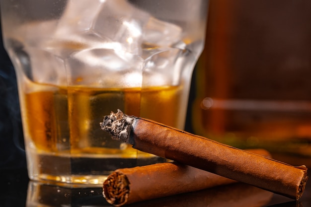 Verre de whisky et cigare allumé sur fond noir