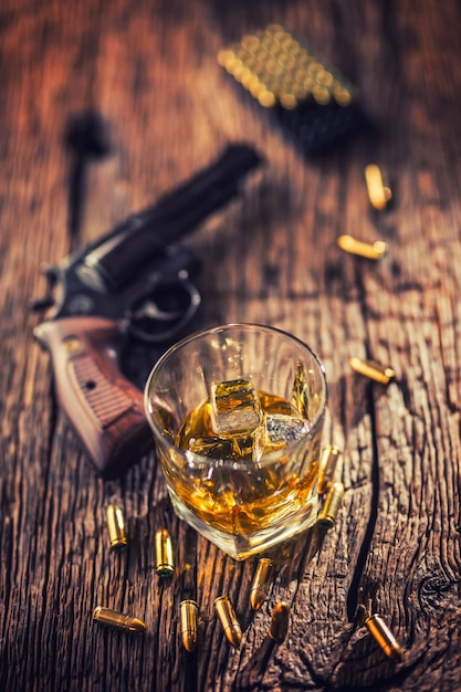 Verre de whisky cognac ou bourbon avec revolver et balles sur table en bois.
