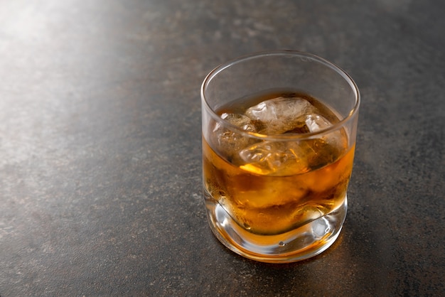 Verre de whisky doré vieilli avec des glaçons sur la table.