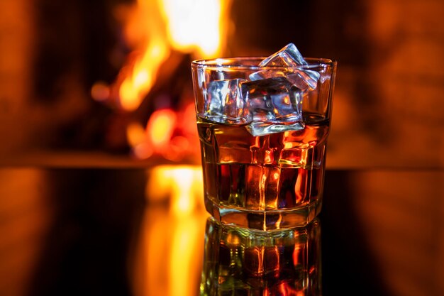 Verre de whisky avec de la glace près de la cheminée