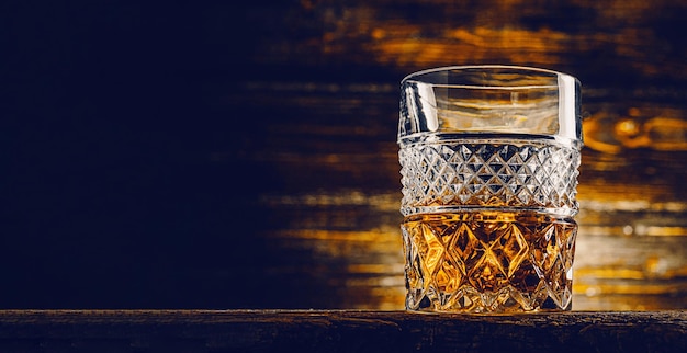 Verre de whisky avec de la glace sur une table en bois entourée de fumée