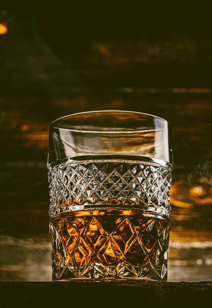 Verre de whisky avec de la glace sur une table en bois entourée de fumée